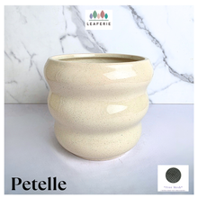 Load image into Gallery viewer, A ceramic planter pot with a wavy, ribbed design in a speckled cream-beige glaze, set against a white marble-patterned background. The brand name 'LEAPERIE' is visible at the top, and the product name 'Petelle' is shown at the bottom left.
