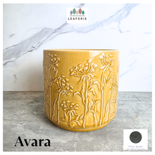 Load image into Gallery viewer, A yellow glazed ceramic planter with embossed wildflower patterns, displayed on a gray stone surface against a white marble background. The brand LEAPERIE is visible at the top, and the product name 'Avara' is shown at the bottom left.