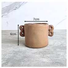 Load image into Gallery viewer, Dovra Brown ceramic planter with handles on a light gray surface, branded 'LEAFERIE'.