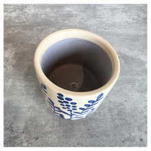 Load image into Gallery viewer, A handmade ceramic planter pot with a blue floral pattern on a cream-colored exterior, shown from a top-down perspective on a gray concrete surface.
