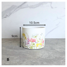 Load image into Gallery viewer, The Leaferie Rhea Two ceramic planters with floral designs on a marble surface, featuring the brand 'LEAFERIE'.