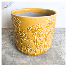 Load image into Gallery viewer, A yellow glazed ceramic planter with embossed wildflower patterns, displayed on a gray stone surface against a white marble background. The brand LEAPERIE is visible at the top, and the product name 'Avara' is shown at the bottom left.