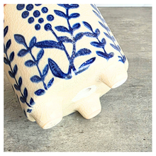 Load image into Gallery viewer, Close-up of a cream-colored ceramic planter with a blue floral and leaf pattern, resting on a gray concrete surface.