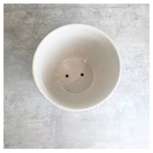 Load image into Gallery viewer, A white ceramic planter pot with a speckled glaze, viewed from directly above. The pot features two drainage holes at the bottom and is placed on a textured gray concrete surface.