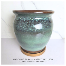 Load image into Gallery viewer, A ceramic planter pot with a speckled green and brown glaze, shown on a light surface with a marble-patterned background. Text at the bottom reads 'MATCHING TRAYS - MATTE TRAY 18CM (TRAYS SOLD SEPARATELY)'.
