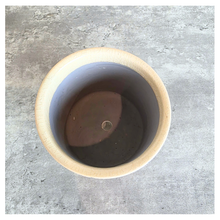Load image into Gallery viewer, A top-down view of a round, unglazed ceramic pot with a light beige exterior and a dark gray interior, set against a textured gray concrete background.