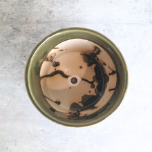 Load image into Gallery viewer, A top-down view of a round ceramic planter or bowl with a glossy olive green rim and a marbled beige and black interior glaze, set against a light gray textured background.