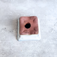 Load image into Gallery viewer, Square ceramic product with a hole on a gray surface, branded 'The Leaferie'.