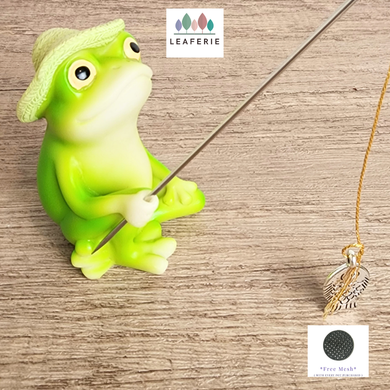 Green frog figurine with a hat holding a stick on a wooden surface, with 'LEAFERIE' branding.