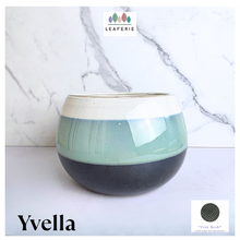 Load image into Gallery viewer, A ceramic planter pot with a two-tone glaze design, featuring a light sage green upper band and a dark charcoal gray lower band, set against a white marble background. The brand name 'LEAFERIE' is visible at the top, and the style name 'Yvella' is at the bottom left.

