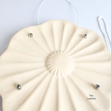 Load image into Gallery viewer, Ysla Cream-colored round cushion with metallic buttons on a white background, branded &#39;The Leaferie&#39;.
