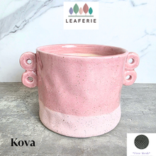 Load image into Gallery viewer, A pink speckled ceramic planter with two loop handles on the sides, shown on a gray stone surface against a white marble background. The brand name LEAFERIE is displayed at the top, and the color name 'Kova' along with a texture swatch graphic are shown in the corners.
