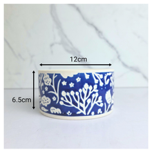 Load image into Gallery viewer, A small cylindrical ceramic container or bowl with a blue and white floral pattern, shown with dimension arrows and labels indicating a width of 12cm and a height of 6.5cm, set against a light marble-patterned background.
