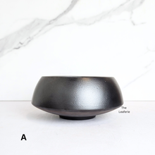 Load image into Gallery viewer, Black ceramic flowerpot on a white marble surface with &#39;The Leaferie&#39; branding.
