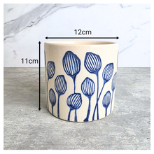 Load image into Gallery viewer, A cylindrical ceramic planter with a blue floral tulip pattern on a cream-colored glaze, shown with black dimension lines indicating a height of 11cm and a width of 12cm against a marble and concrete background.
