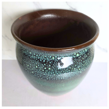 Load image into Gallery viewer, A ceramic planter pot with a glossy dark brown rim and a speckled green glaze that fades to black at the base, set against a light marble-patterned background.

