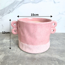Load image into Gallery viewer, A pink speckled ceramic planter with two loop handles on the sides, shown on a gray stone surface against a white marble background. The brand name LEAFERIE is displayed at the top, and the color name 'Kova' along with a texture swatch graphic are shown in the corners.
