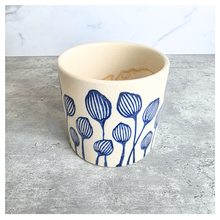 Load image into Gallery viewer, An off-white ceramic planter with a blue hand-painted pattern of stylized flowers, displayed on a gray surface against a white marble background. The brand LEAFERIE is visible at the top, and the name 'Zorina' is shown at the bottom left.background.
