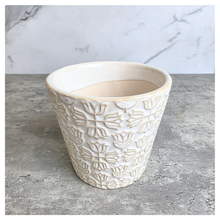 Load image into Gallery viewer, An off-white ceramic planter with a textured, embossed floral pattern, displayed on a gray stone surface against a white marble background. The brand name 'LEAFERIE' is visible at the top, and the product name 'Colette' is shown at the bottom left.
