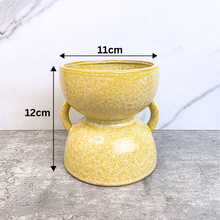 Load image into Gallery viewer, A yellow speckled ceramic planter pot with a wide top bowl, two side handles, and a flared base, shown on a gray surface against a white marble-patterned background with dimension labels of 11cm width and 12cm height.
