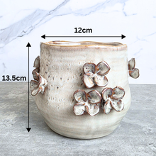 Load image into Gallery viewer, A ceramic planter with raised flower details, shown with dimension overlays indicating a height of 13.5cm, width of 12cm, and depth of 12cm against a marble and concrete background.
