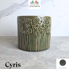 Load image into Gallery viewer, A cylindrical ceramic planter in a glossy olive green glaze with embossed floral and stem patterns, shown on a gray stone surface against a white marble background. The brand name LEAFERIE is visible at the top, and the color name 'Cyris' is shown at the bottom left.
