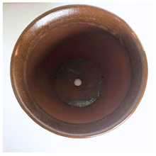 Load image into Gallery viewer, Top-down view of a round ceramic planter pot with a glossy brown and bronze finish, featuring a single drainage hole in the center, set against a plain white background.
