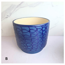 Load image into Gallery viewer, A blue ceramic planter with a raised leaf pattern and a cream-colored interior, set against a white marble-patterned background.
