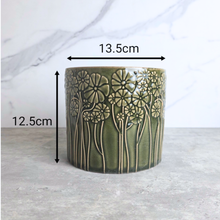 Load image into Gallery viewer, An olive green ceramic planter with a raised floral pattern, shown with black dimension arrows and text indicating a width of 13.5cm and a height of 12.
