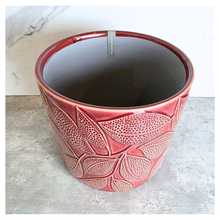 Load image into Gallery viewer, Talia Red ceramic planter with leaf pattern on a gray surface, branded 'LEAFERIE'.
