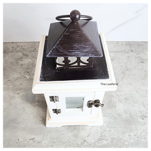 Load image into Gallery viewer, Decorative lantern with black top and white base on a gray surface, branded &#39;The Leaferie&#39;.
