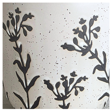 Load image into Gallery viewer, Close-up of a speckled off-white ceramic surface with dark charcoal floral silhouettes and small black dots.
