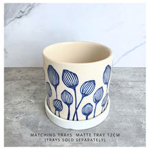 Load image into Gallery viewer, An off-white ceramic planter with a blue hand-painted pattern of stylized flowers, displayed on a gray surface against a white marble background. The brand LEAFERIE is visible at the top, and the name 'Zorina' is shown at the bottom left.
