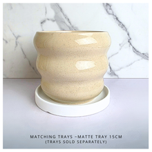 Load image into Gallery viewer, A ceramic planter pot with a wavy, ribbed design in a speckled cream-beige glaze, set against a white marble-patterned background. The brand name 'LEAPERIE' is visible at the top, and the product name 'Petelle' is shown at the bottom left.
