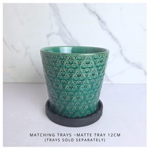 Load image into Gallery viewer, A green glazed ceramic cup with an embossed geometric trellis pattern, resting on a round black saucer. The background is a white marble-patterned surface with a white tabletop.
