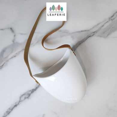 The Leaferie PAtina hanging planter. material ceramic.white colour with leather strap. no drainage hole. front view